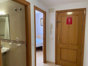 A hotel room with a wooden door, a bathroom with a sink and mirror, and a bed in the background. - Apartamento Isabel - Apartamento en Vinaròs - Ref. 832 (Vinaròs)
