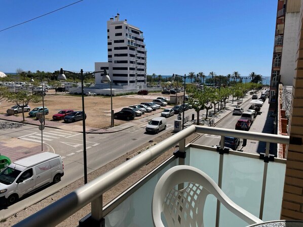 A balcony with a view of a street, parked cars, and a tall building in the background. - Apartamento Isabel - Apartamento en Vinaròs - Ref. 832 (Vinaròs)