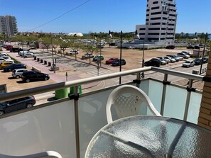 A balcony with a glass table and chairs, overlooking a parking lot with several cars and a building in the background. - Apartamento Isabel - Apartamento en Vinaròs - Ref. 832 (Vinaròs)