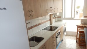 Une cuisine dotée de meubles en bois, d’un évier en acier inoxydable, d’un four encastré et d’un lave-linge.