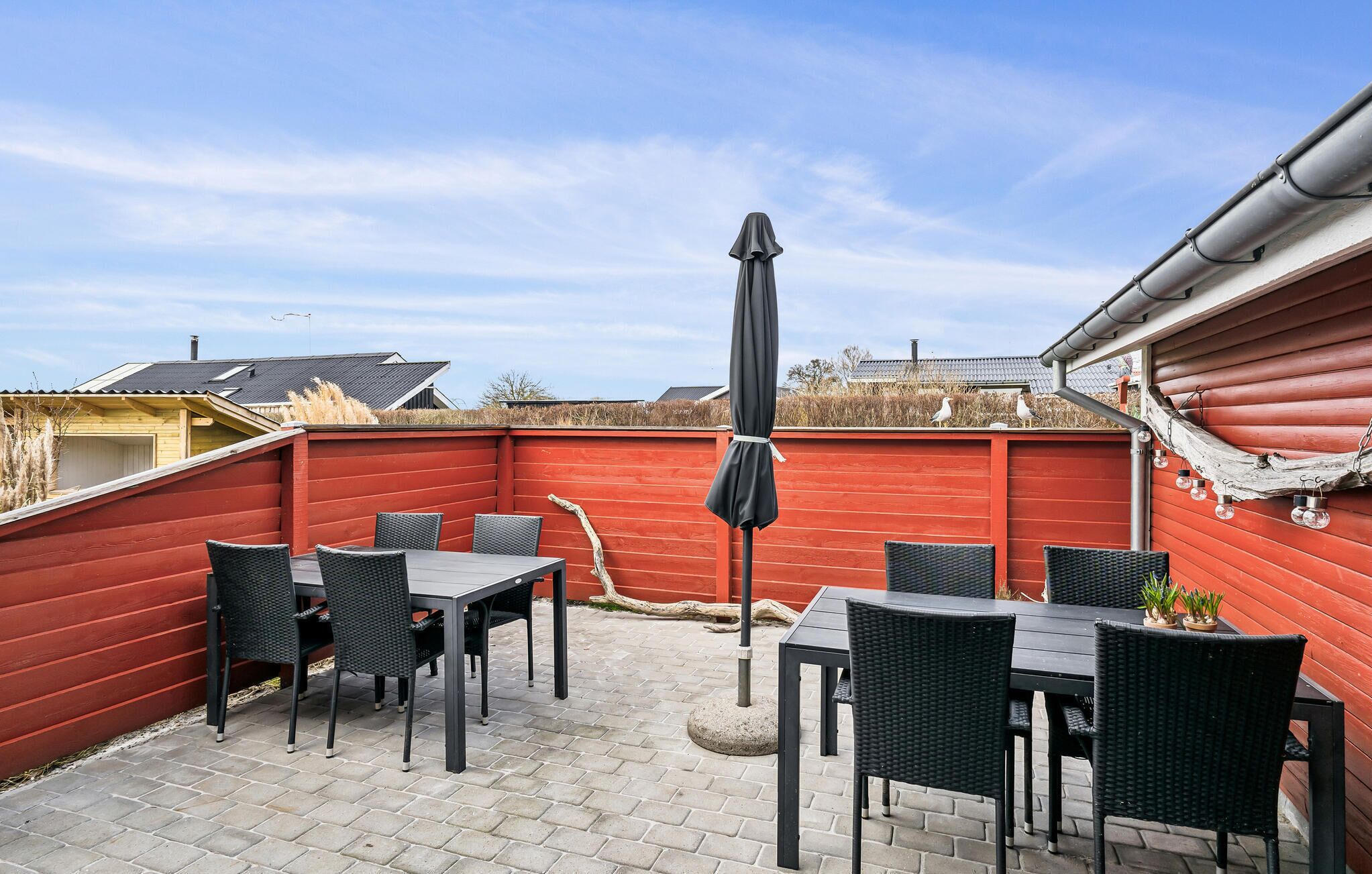 An outdoor patio with a red wall, a black umbrella, and wicker furniture.