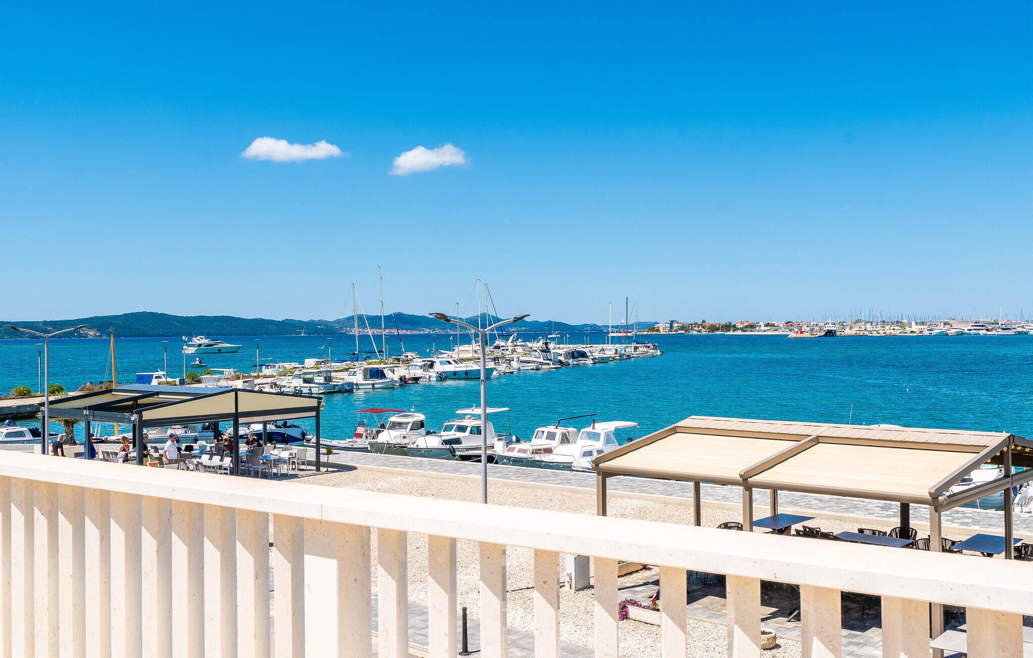 A marina with boats docked, a clear blue sky, and a distant cityscape.
