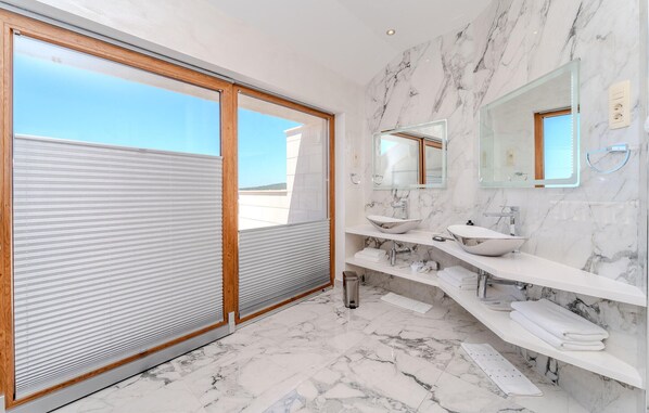 Une salle de bain moderne dotée d’une grande porte coulissante en verre, de deux vasques, d’un miroir et d’un revêtement de sol en marbre.