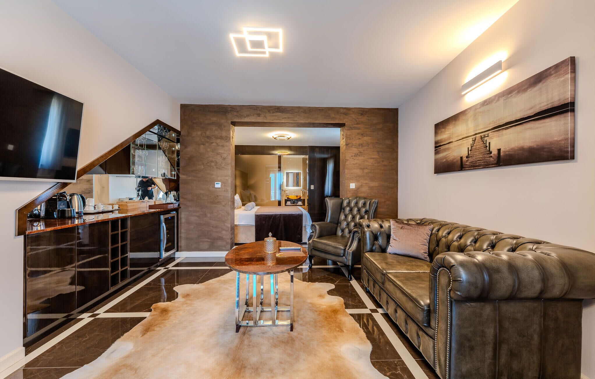 A modern living room with a leather sofa, a coffee table, and a flat-screen TV mounted on the wall.