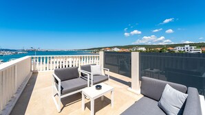 A balcony with a view of the sea, a white railing, and two grey sofas with cushions.