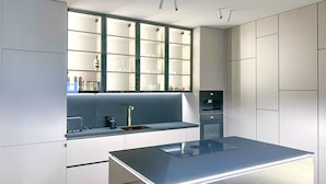 A modern kitchen with a central island, built-in appliances, and a window with shelves.