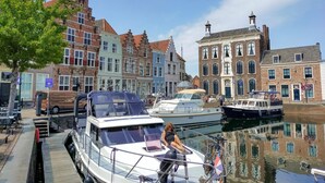 A canal with boats docked, a woman sitting on a boat, and buildings along the water. - Beautiful home in Heinkenszand (Heinkenszand)