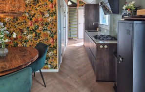 A kitchen with a wooden floor, a dining table with chairs, a stove, and a wall with a floral pattern. - Beautiful home in Heinkenszand (Heinkenszand)