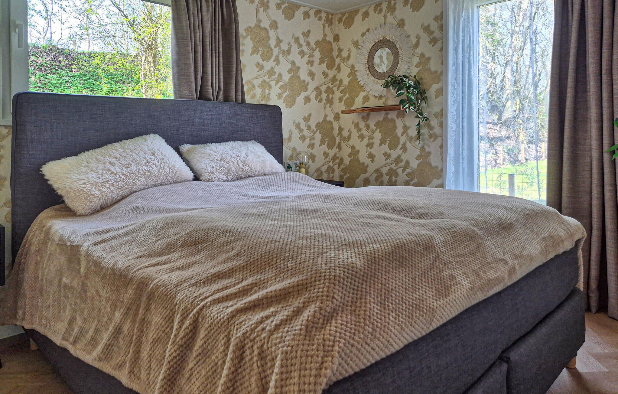 Un lit avec une tête de lit grise, deux oreillers moelleux et une couverture tricotée de couleur beige.