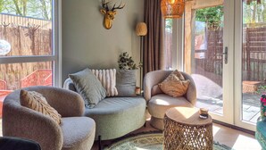 A cozy living room with a sofa, armchairs, a small round table, a decorative deer head, and a large window with a view of a wooden fence. - Beautiful home in Heinkenszand (Heinkenszand)