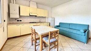 A compact kitchen with a dining table and chairs, a blue sofa, and a tiled floor. - Aleksandra 4-Carraro Immobiliare Jesolo (Lido di Jesolo)