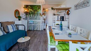 En hyggelig stue med en sofa, et spisebord med stole, et lille rundt bord med en plante og et hvidt hegn med teksten 