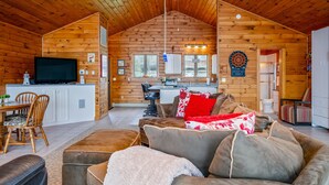 L’intérieur d’une cabane en rondins comprend un coin repas, une cuisine et un salon aménagé avec des canapés et un téléviseur.
