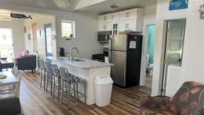 A modern kitchen with a central island, bar stools, a refrigerator, and a microwave.