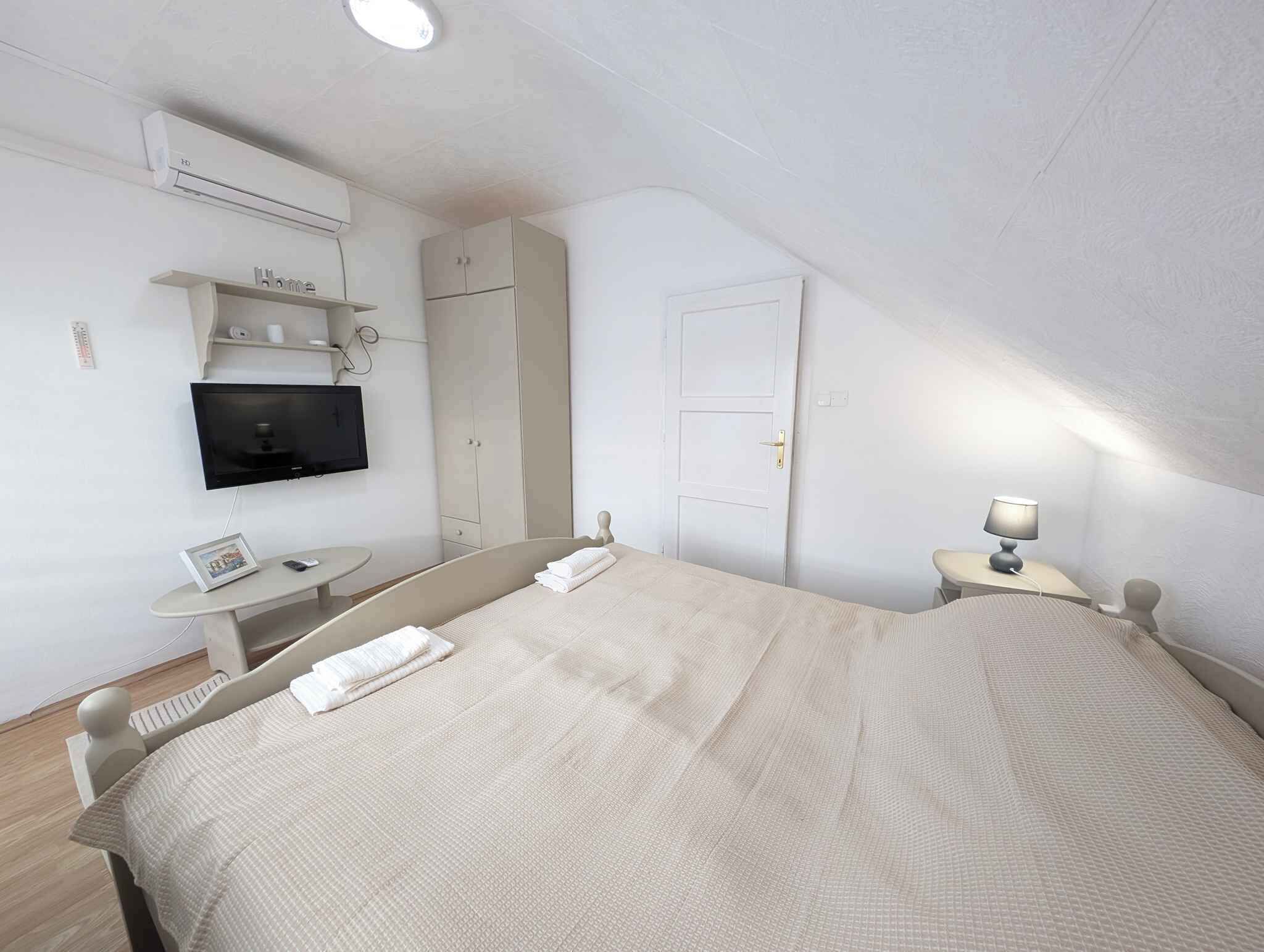 Ein Schlafzimmer mit Bett, Fernseher, Schreibtisch, Kleiderschrank und einer Tür.