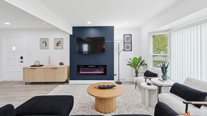 Una sala de estar moderna con chimenea, televisor de pantalla plana y un ventanal con persianas.