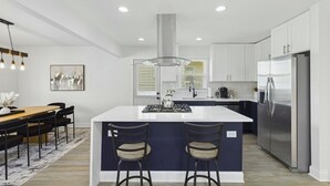 Una cocina moderna con una isla central, electrodomésticos de acero inoxidable y un comedor con mesa y sillas.