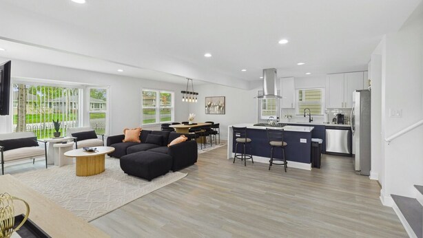 Una sala de estar moderna con un sofá negro, un comedor y una cocina con barra.
