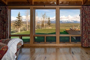 A room with a large window, wooden floor, and a bed with a patterned blanket.