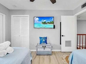 A bedroom with two beds, a TV on the wall, a suitcase, and a door leading to another room.
