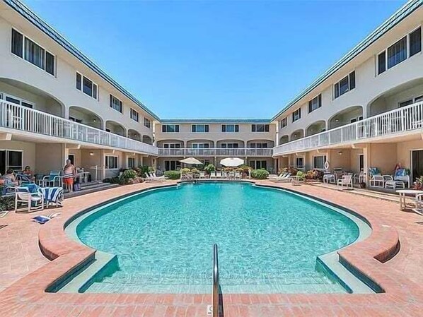A pool area with a central pool, lounge chairs, and a multi-level building with balconies.