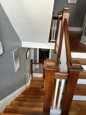 Staircase leads to an upper floor with polished wood floors and framed pictures on the wall.