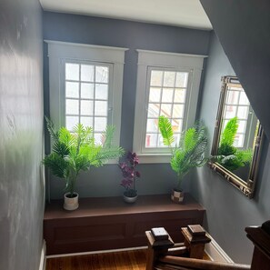 Plants adorn the window sill, complemented by a mirror and a staircase with a dark finish.