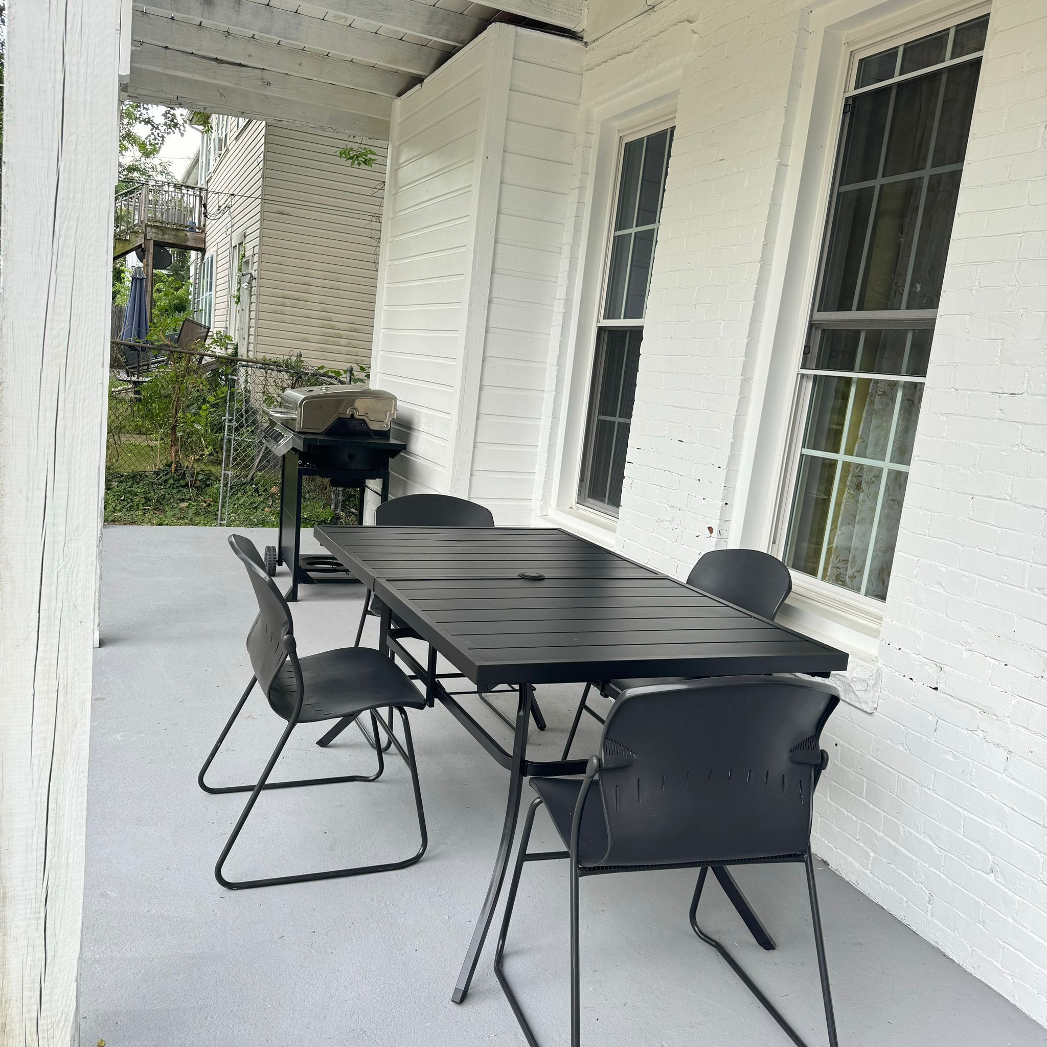 A covered patio with a black metal table and chairs, a grill, and a white brick wall.
