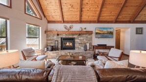 A cozy living room with a stone fireplace, leather sofas, and wooden beams on the ceiling. - Hillcrest at Tahoe Donner by Tahoe Getaways - 3BR Pet-Friendly w/ Pool Table & Ping Pong (Truckee)