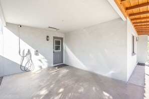 Un espace extérieur abrité, doté d’un sol en béton, d’une porte et d’un luminaire fixé au mur.