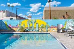 A swimming pool with a mural of cacti and desert landscape, surrounded by lounge chairs and a clear sky.