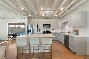 A modern kitchen with a central island, bar stools, stainless steel appliances, and a view to the outside.