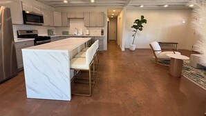 Une cuisine moderne dotée d’un îlot en marbre, d’appareils électroménagers en acier inoxydable et d’un coin repas avec une chaise et une table blanches.