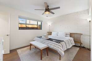 Une chambre à coucher avec un lit, un banc, un ventilateur de plafond et une vue sur l’extérieur par une fenêtre.