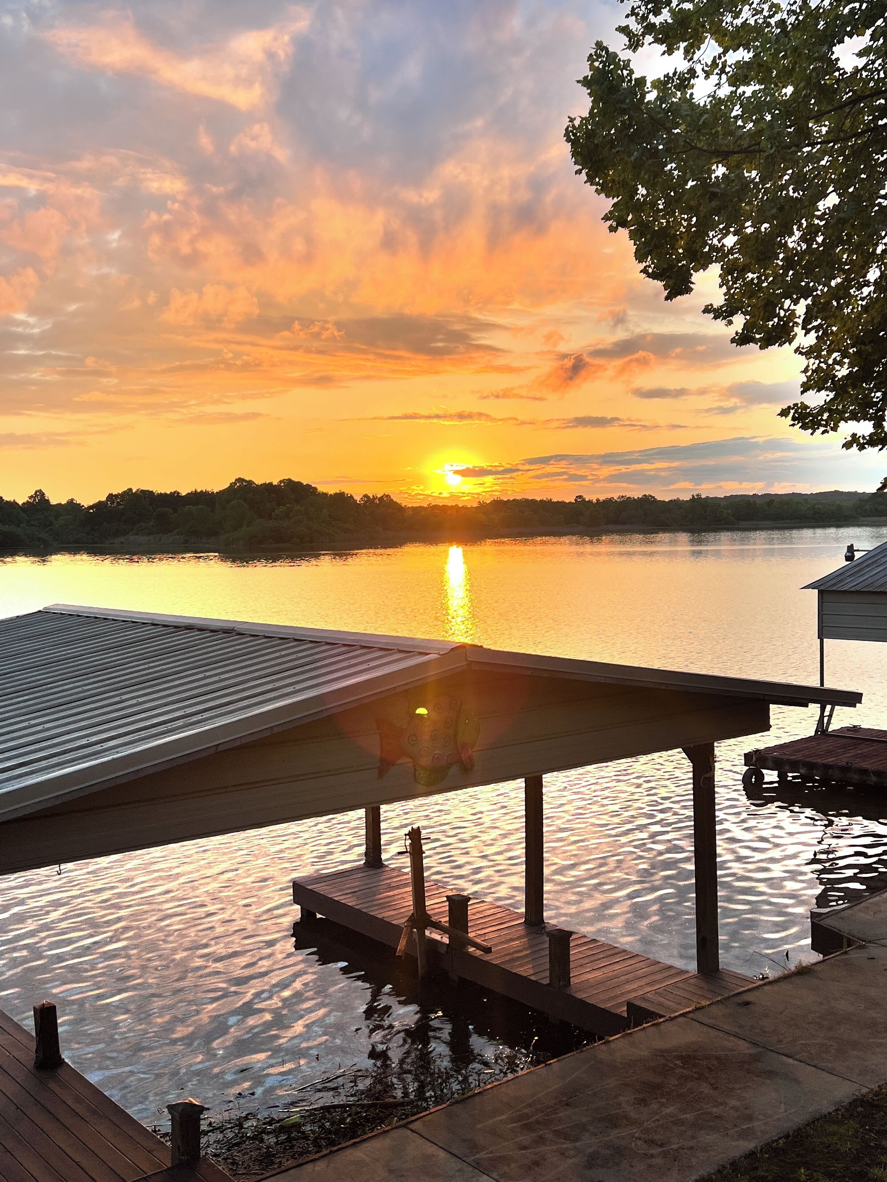A wooden dock extending into a calm lake with a sunset in the background.