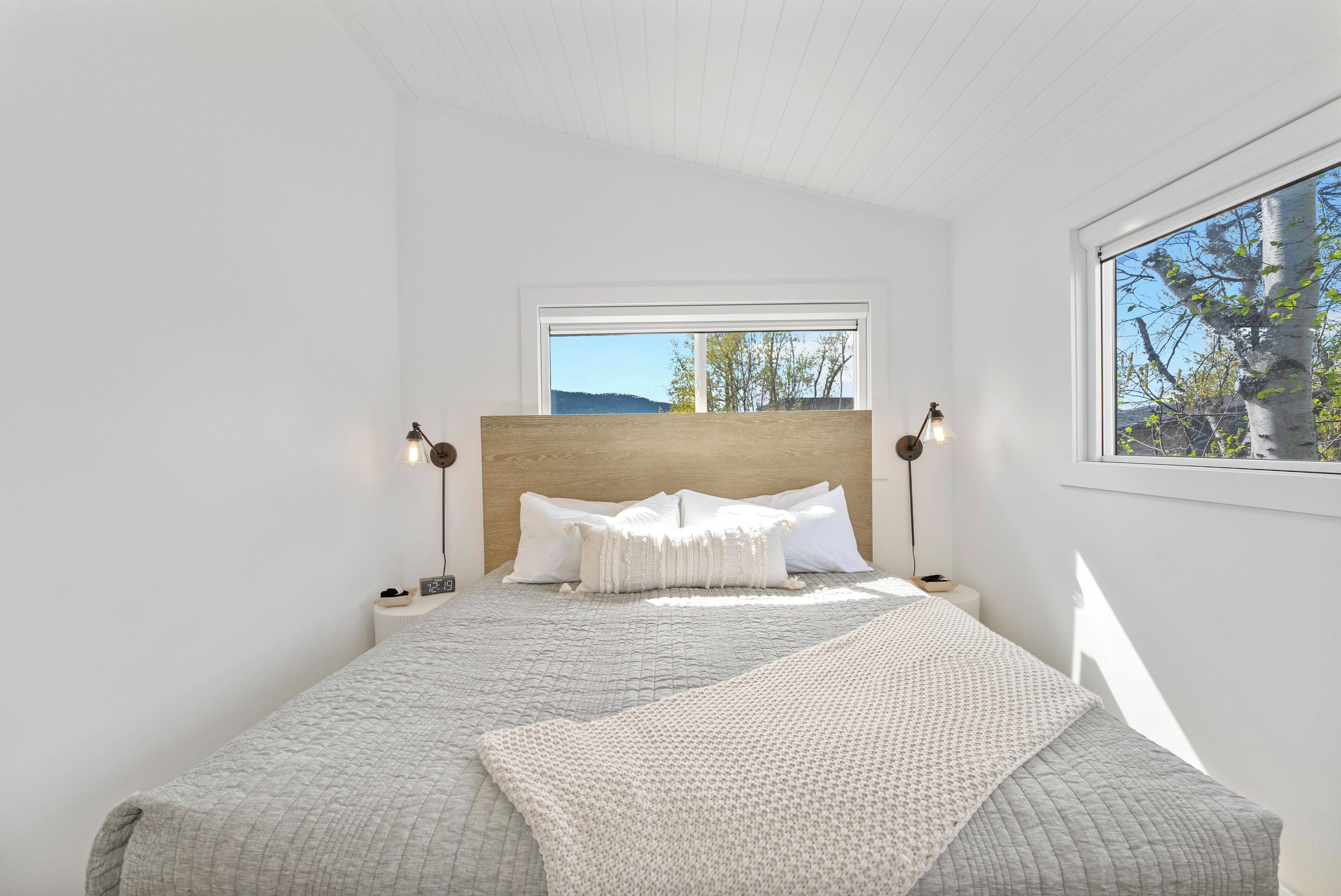 Een slaapkamer met een groot bed, een raam met uitzicht op bomen, en een houten hoofdeinde.