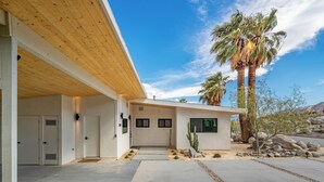 A modern house with a wooden overhang, a concrete driveway, and a desert landscape with cacti and a palm tree. - Palm Springs Haven / Pool, Hot Tub & Mountain Views (Palm Springs)