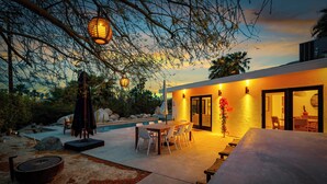 A modern outdoor patio with a pool, dining area, and a well-lit entrance. - Palm Springs Haven / Pool, Hot Tub & Mountain Views (Palm Springs)