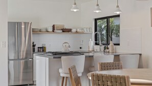 A modern kitchen with a stainless steel refrigerator, white cabinetry, and a central island with chairs. - Palm Springs Haven / Pool, Hot Tub & Mountain Views (Palm Springs)