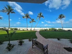 A paved pathway leading to a bench overlooking a beach with palm trees and a clear blue sky. - Amazing Gulf views from the10th floor Beach front 2/2 condo at Riviera Club (Fort Myers Beach)