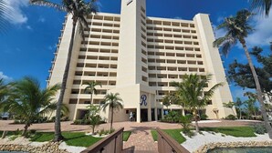 A large hotel with multiple floors, a central entrance, and a pool area with palm trees.