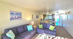 A living room with a sofa, a coffee table, and a ceiling fan. There is a kitchen area in the background. - Amazing Gulf views from the10th floor Beach front 2/2 condo at Riviera Club (Fort Myers Beach)