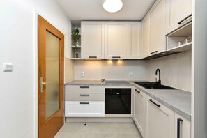 Una cocina compacta con muebles blancos, horno integrado y una encimera con fregadero.