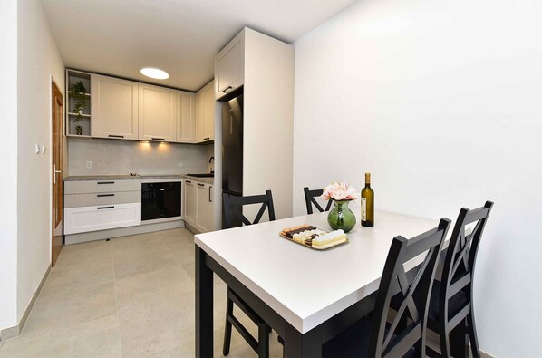 Une cuisine moderne avec des armoires blanches, un lave-vaisselle intégré et un coin repas comprenant une table blanche et des chaises noires.