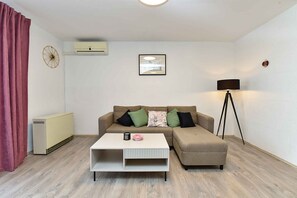 Un salón con sofá, mesa de centro, lámpara de pie, radiador y un reloj en la pared.