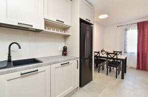 A modern kitchen with a built-in refrigerator, a coffee machine, and a dining area with a table and chairs.