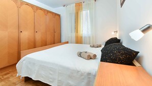 A bedroom with a large bed, a wooden wardrobe, a nightstand, and a wall-mounted lamp. - Holiday apartment with balcony and air conditioning (Fažana)