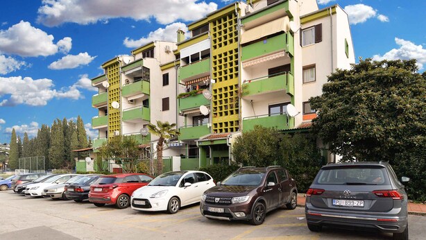 A multi-story residential building with balconies, parked cars, and a clear blue sky. - Holiday apartment with balcony and air conditioning (Fažana)