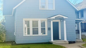 A two-story house with a front porch, a garage door, and a small front yard. - Spacious Family Fun Retreat 3 min to Beach/Zoo/Outlet Fenced Backyard w/ Deck (Michigan City)