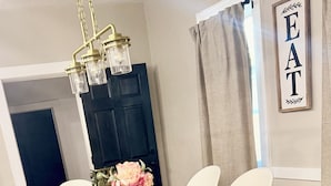 A dining area with a wooden table, white chairs, and a chandelier. - Spacious Family Fun Retreat 3 min to Beach/Zoo/Outlet Fenced Backyard w/ Deck (Michigan City)